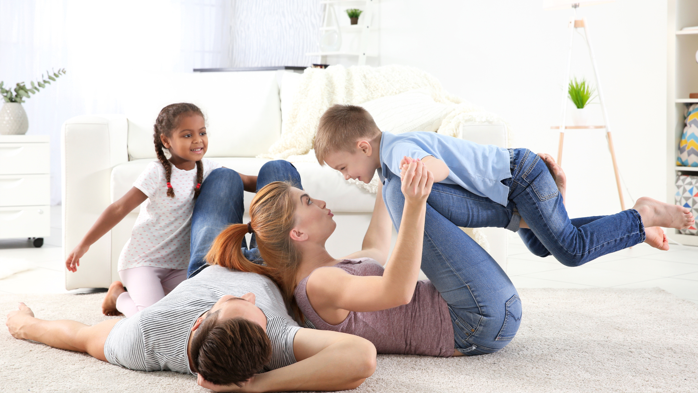 A Mother and a Father playing with their Son and Daughter on the floor of their home.